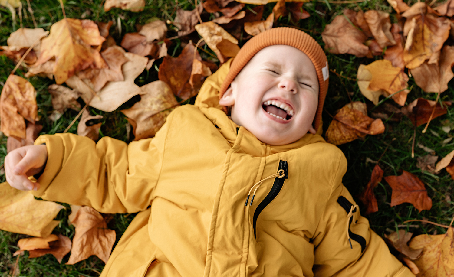 Ett glatt barn ligger på höstlöven och skrattar.