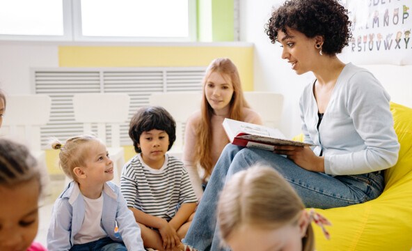 En mörkhyad lärare sitter med barnen och läser.