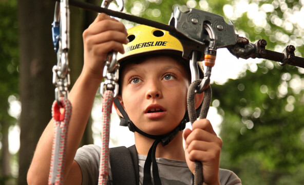 En ung pojke fäster linbanans rep medan han bär hjälm.
