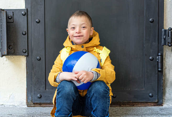 En handikappad pojke flinar och håller en boll i knät.
