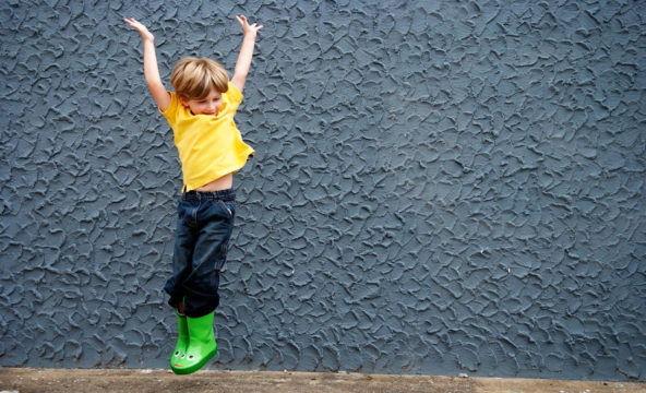 Poika hyppii tasajalkaa kädet ilmassa harmaan seinän edessä.