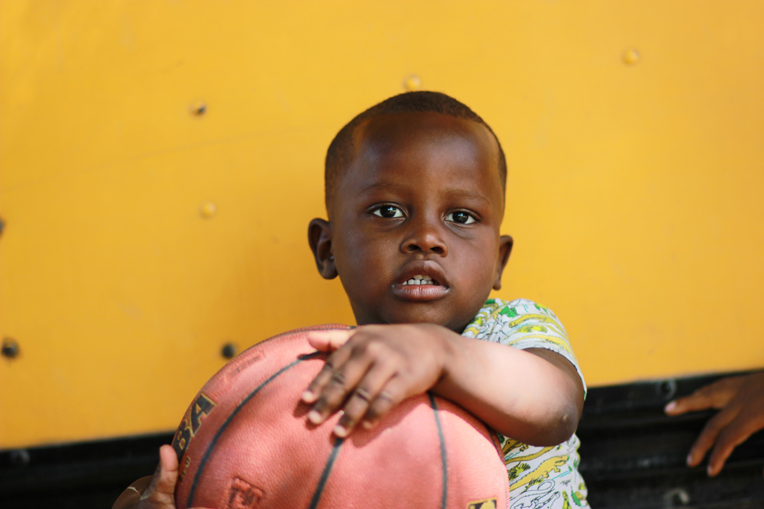 Tummaihoinen, pieni lapsi pitää käsissään koripalloa.
