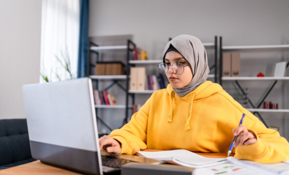 Huivipäinen nuori nainen istuu tietokoneen edessä.
