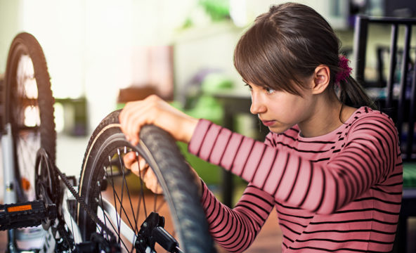 På bilden reparerar en ung person ett cykelhjul och ser koncentrerad ut.