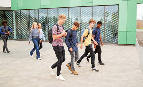 A group of young people walking past a modern-looking school building.