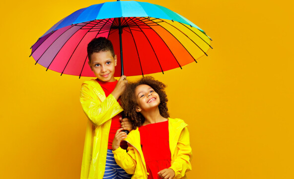 Kaksi iloista lasta sateenkaarisateenvarjon alla.