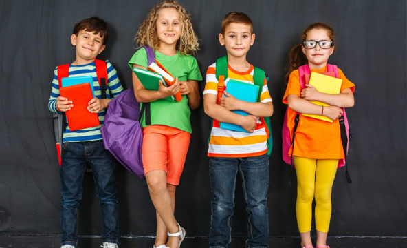 Lapsen oikeuksien viikko 2020: Neljä värikkäästi pukeutunutta koululaista liitutaulun edessä kirjat sylissään.
