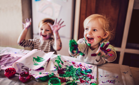 Kuvassa kaksi lasta leikkii innostuneen oloisina sormiväreillä
