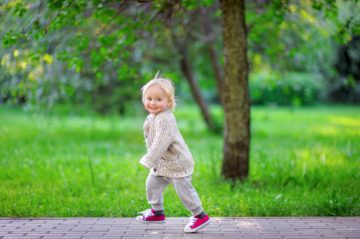 Kuvassa vaaleisiin vaatteisiin puettu lapsi juoksee kävelypolulla. Taustalla erottuu vihreää nurmea ja puu.