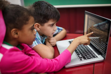 En flicka och pojke använder datorn tillsammans.