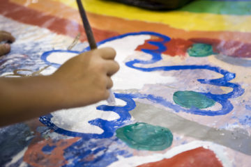 Lapsen käsi maalaa valkoista kyyhkyä muraalille.