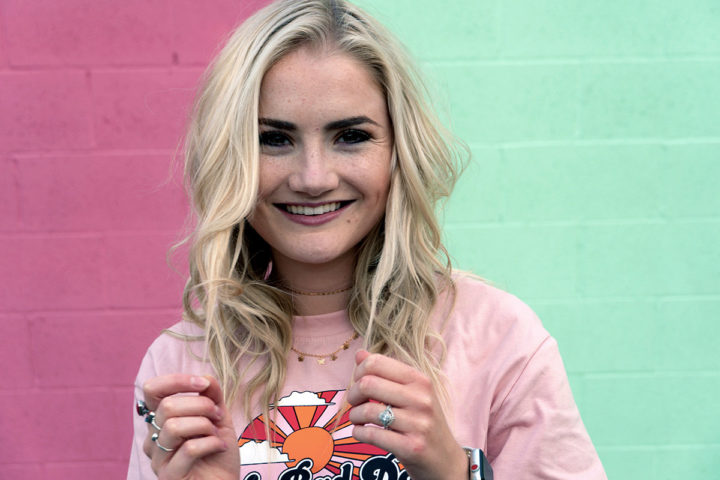 A happy young girl with freckles stands in front of a half-pink and half-green wall.