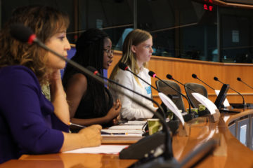 Kolme nuorta naista istuu valtuustossa mikrofonit edessä.