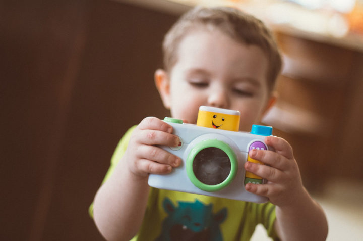 Leikki-ikäinen lapsi pitää lelukameraa käsissään ja tähtää sillä valokuvan ottajaa.