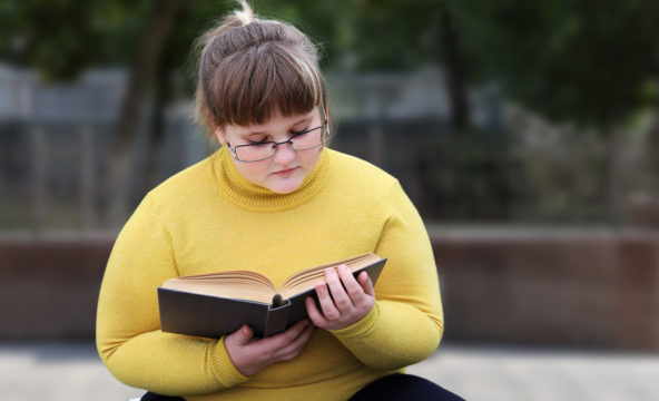 Pyöreähkö nuori tyttö lukee kirjaa penkillä.