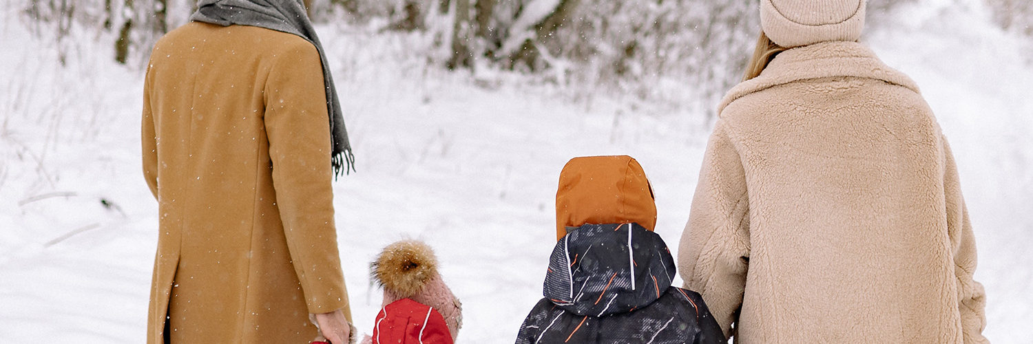 Nelihenkinen perhe kävelee lumessa selin kameraan.