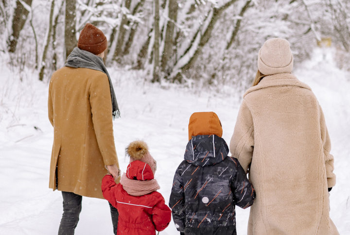 Nelihenkinen perhe kävelee lumessa selin kameraan.
